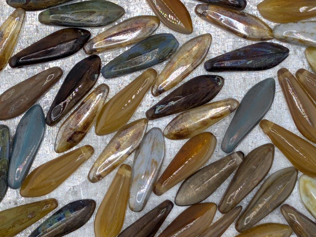 a collection of various colored glass beads or stones, including shades of brown, gray, and blue, arranged in a scattered pattern.