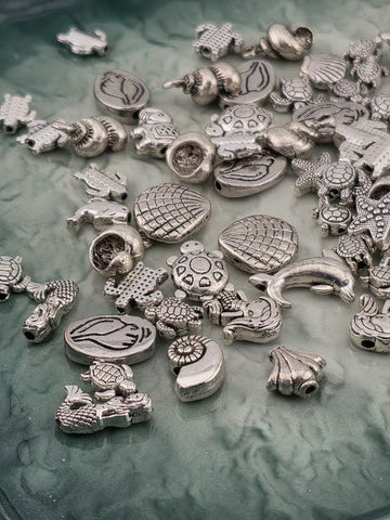 various silver-colored metal charms, including sea creatures such as fish, shells, and sea creatures, scattered across a surface.