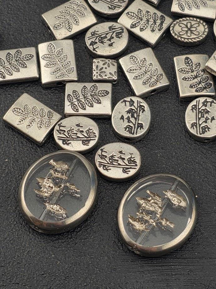 a collection of various metal beads and buttons with intricate designs, including leaves and floral patterns, scattered on a dark surface.