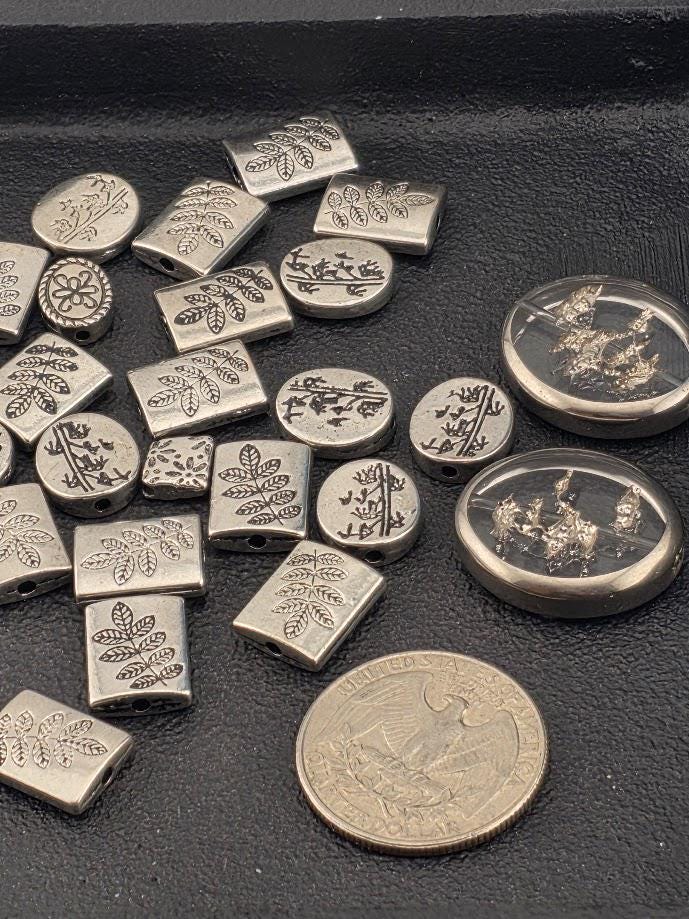 a collection of various metal beads and coins, including a quarter, arranged on a dark surface.