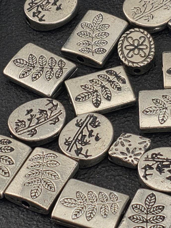 various metal beads with leaf and flower designs, arranged on a dark surface.