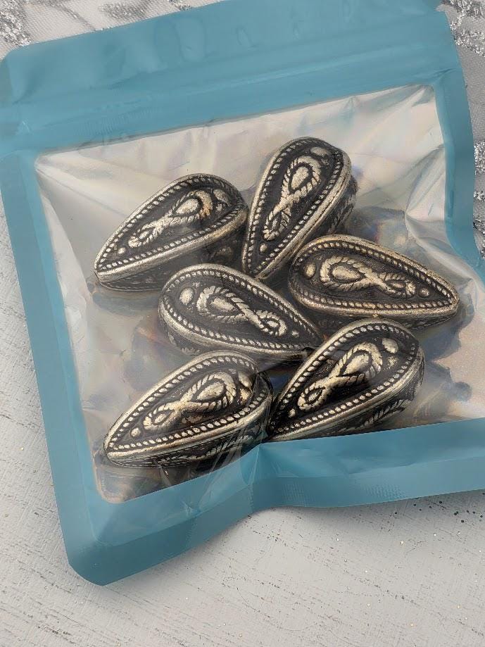 A clear plastic bag containing several silver-colored metal beads with intricate designs.