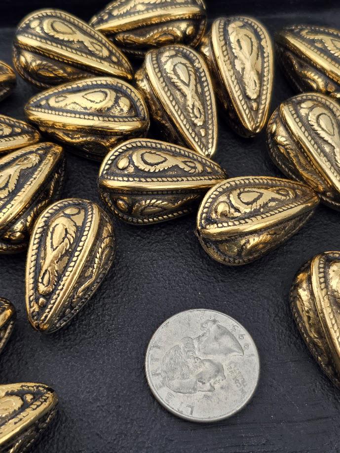 a collection of ornate, golden-colored metal beads arranged on a dark surface, with a silver coin placed in the foreground.
