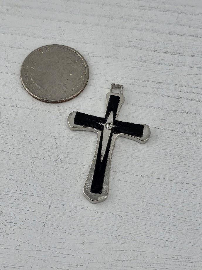 A silver cross pendant is displayed in a black box with a gold ribbon bow.