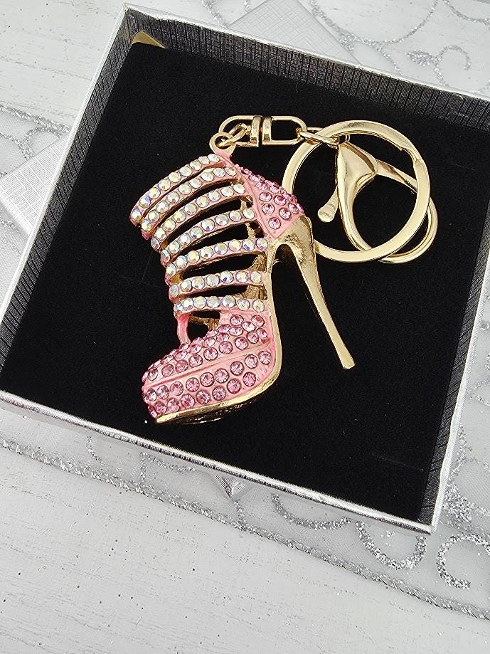 A pink high-heeled shoe keychain with rhinestones and a gold-colored keyring is displayed in a black box.