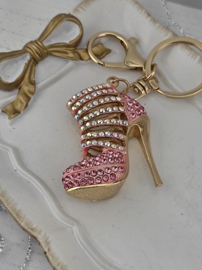 A keychain with a pink high-heeled shoe adorned with rhinestones, placed on a white surface.