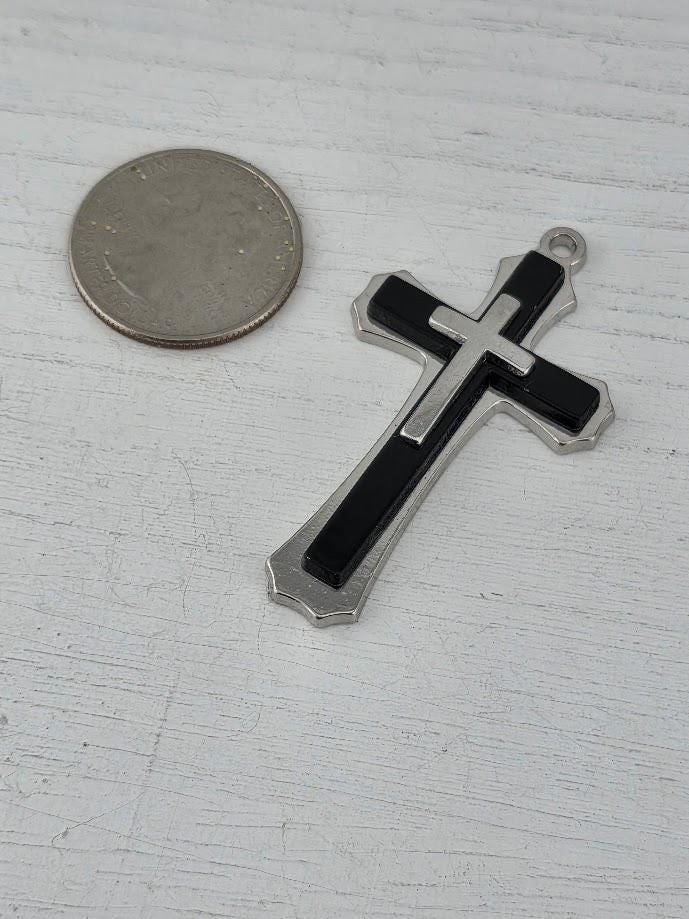 A silver and black cross pendant is displayed in a silver box with a gold ribbon bow.
