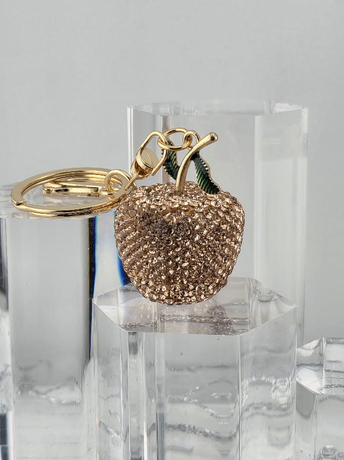 A gold-colored keychain with a small, intricately designed apple charm made of sparkling rhinestones or crystals.