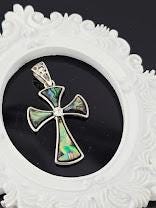 A silver-toned pendant cross with colorful inlays is displayed in a blue gift box, with a silver clasp and a white ribbon bow.