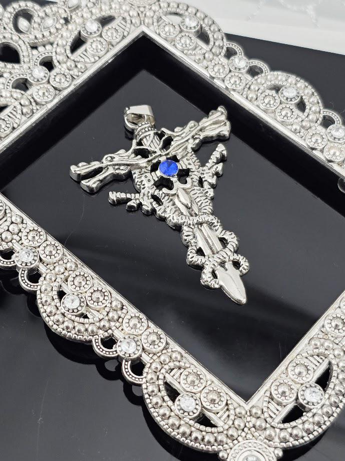 A silver-colored pendant with intricate designs and a blue gemstone is displayed in a black box with a gold ribbon.
