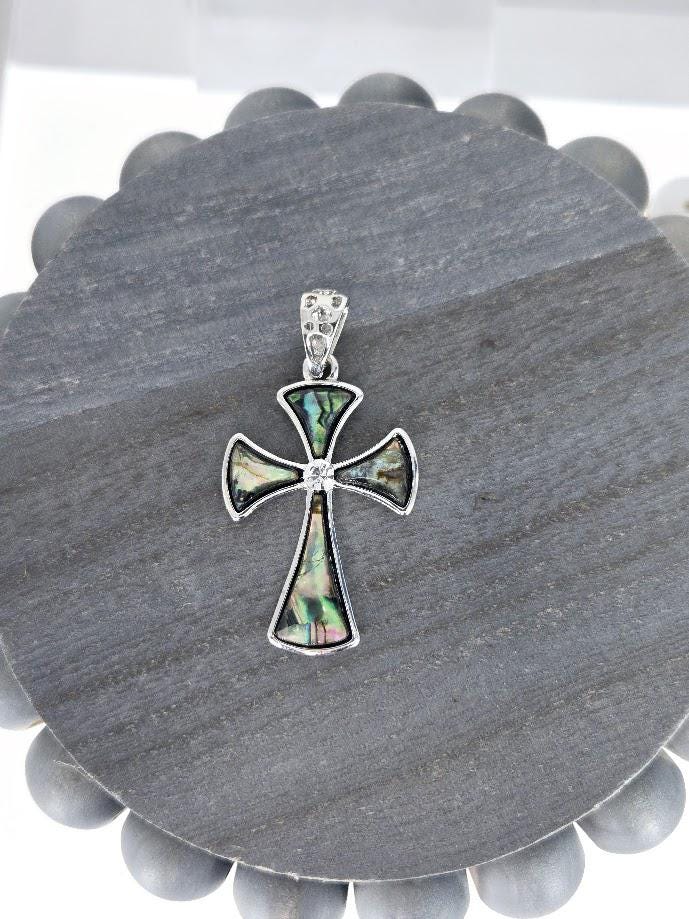 A silver cross pendant with a colorful, abstract design is displayed on a gray circular surface.