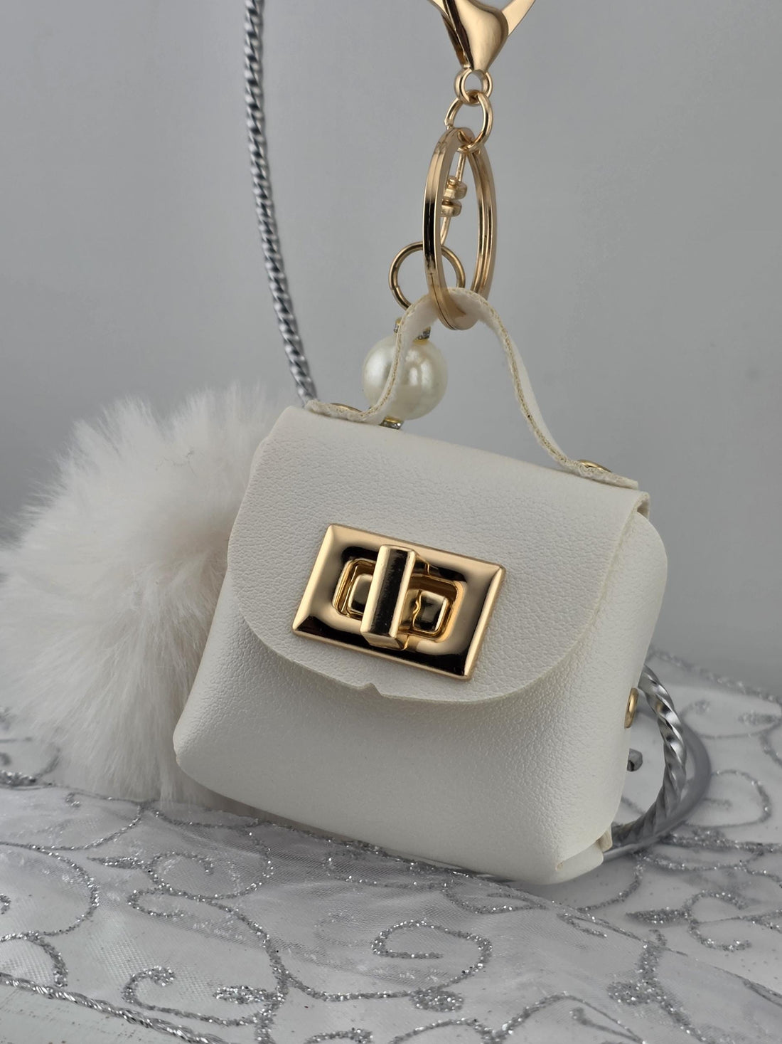 A white leather handbag with a gold lock and keychain attached to it.