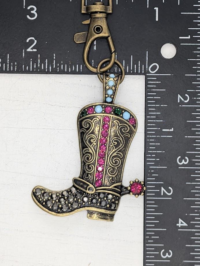 A decorative keychain in the shape of a cowboy boot, adorned with colorful gemstones and a metal clasp.