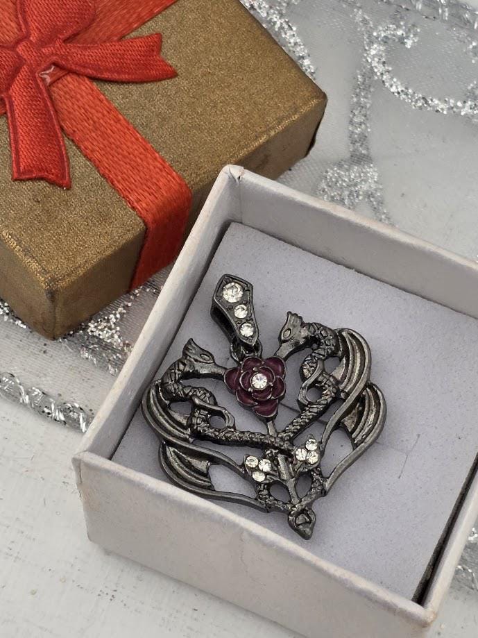 A decorative brooch with a floral design and sparkling gemstones is displayed in a white box, accompanied by a gift box with a red ribbon.