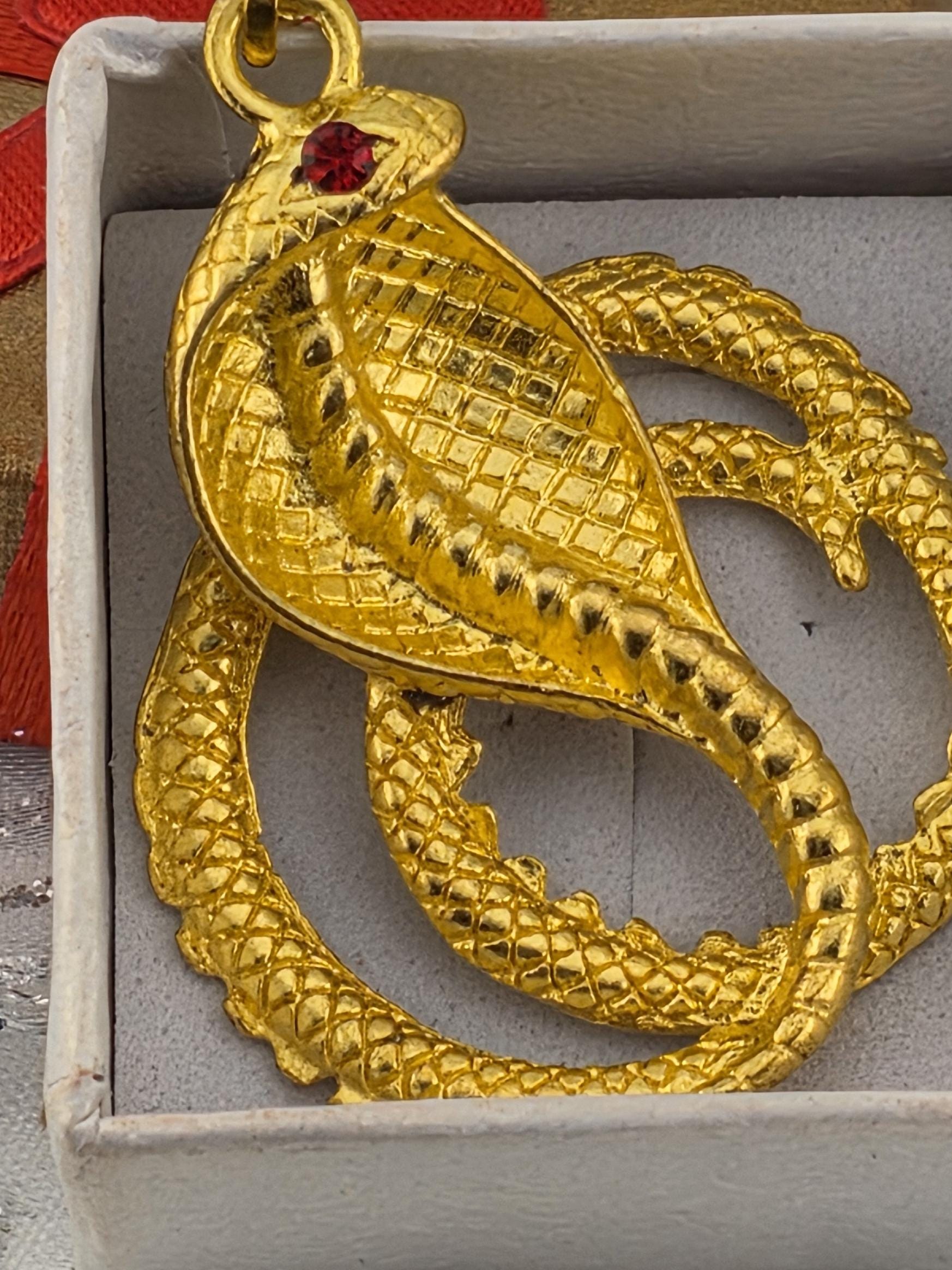A close-up view of a golden snake-shaped pendant with a red gemstone on its head.