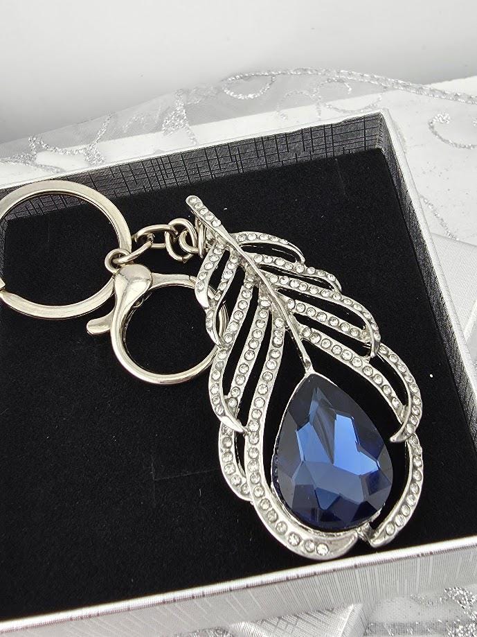 A silver keychain with a large blue gemstone in the shape of a feather.