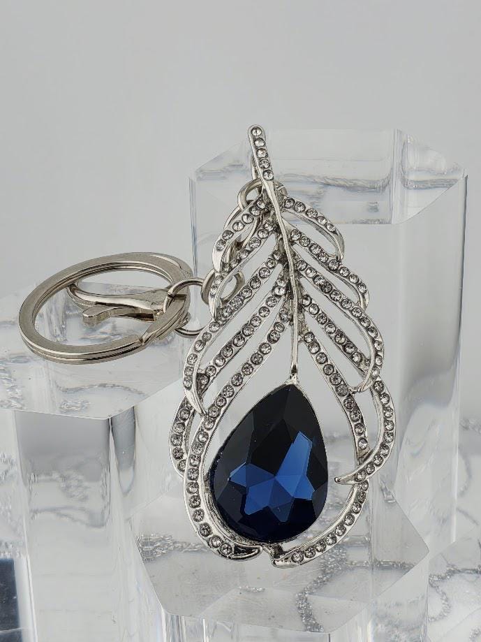 A silver keychain with a large blue gemstone in the center, surrounded by a decorative leaf-like design.