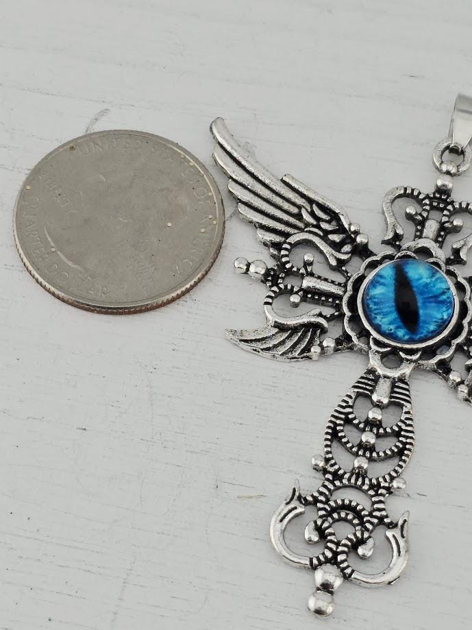 A silver-toned pendant with intricate designs, including a blue eye-shaped gemstone, is placed next to a United States quarter coin on a white surface.