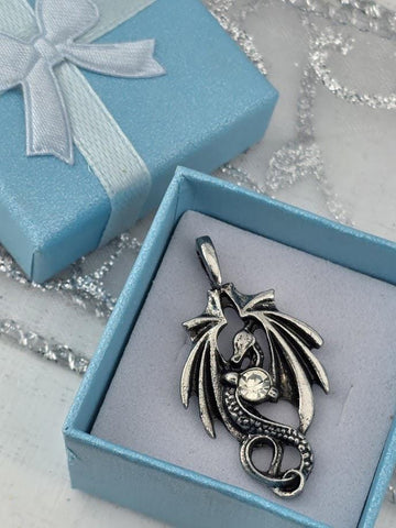 A silver pendant in the shape of a dragon is displayed in a blue gift box with a white ribbon bow.