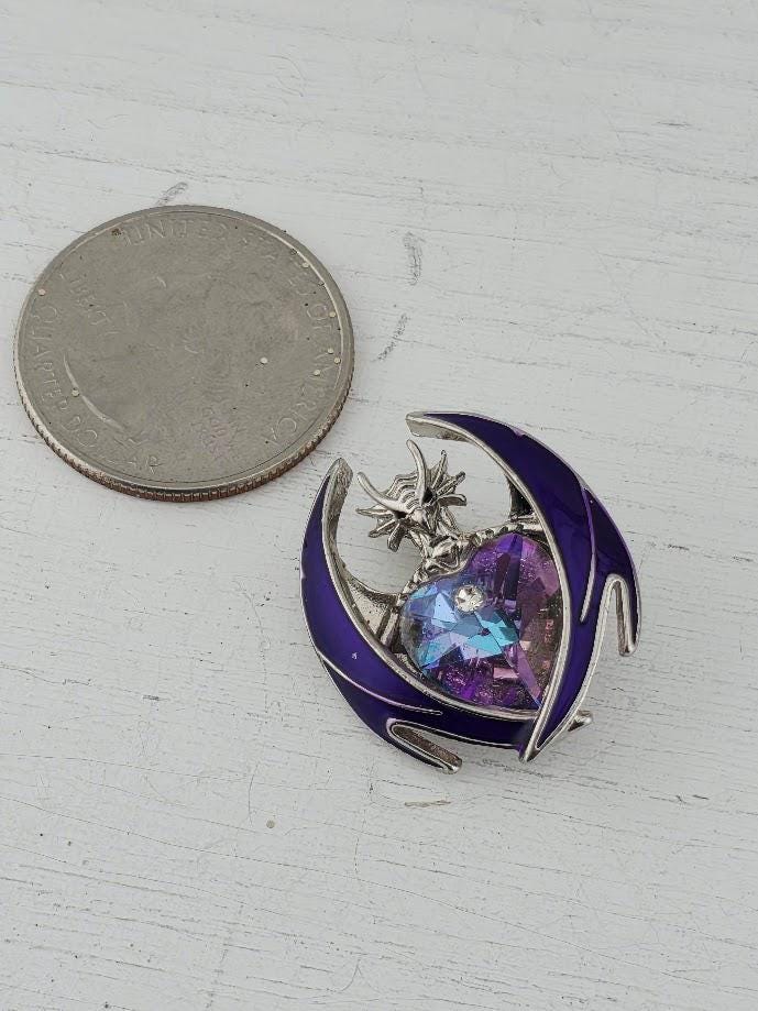 A silver coin next to a purple and blue pendant with a dragon design.