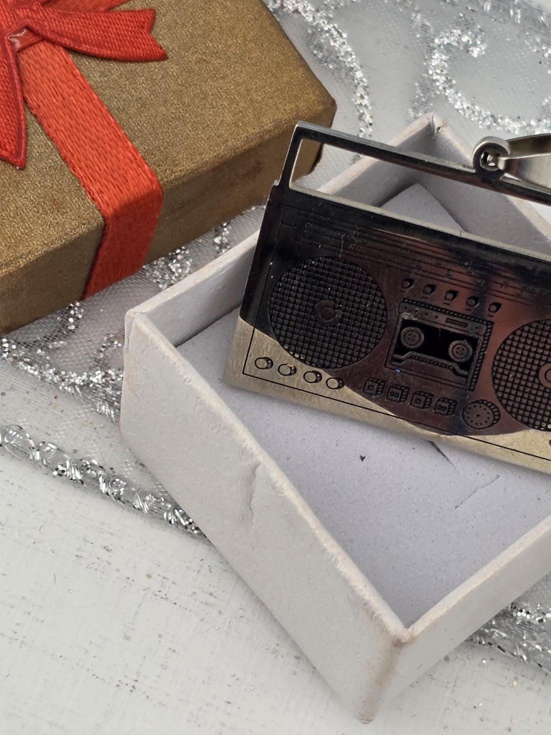 a small, metallic object resembling a boombox or radio, placed on top of a brown gift box with a red ribbon.