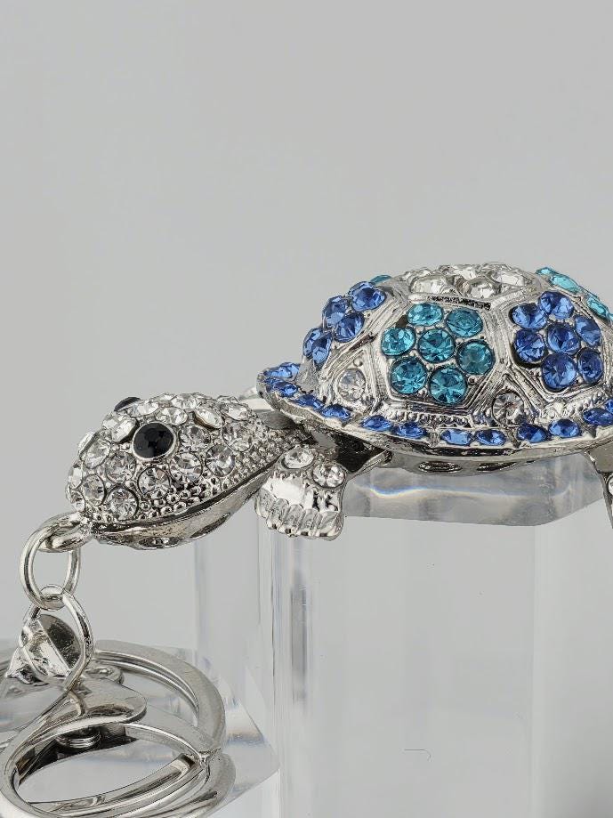 A silver-colored keychain with a turtle-shaped design, adorned with blue and white gemstones.