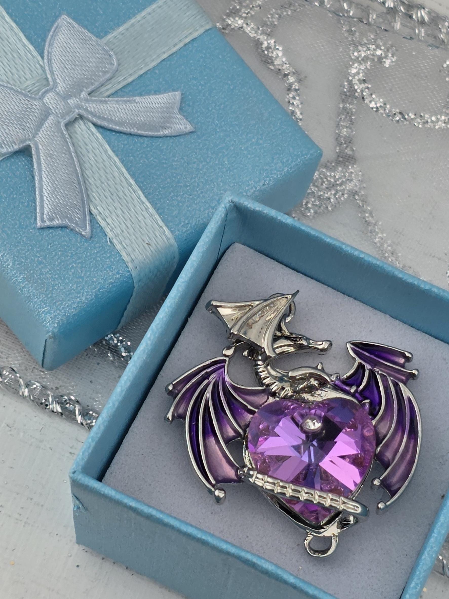 A blue gift box with a silver and purple decorative piece inside, placed on a white surface with silver and white tinsel.