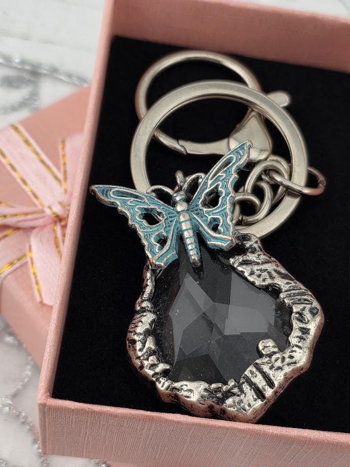 A keychain with a silver butterfly charm and a large black gemstone in the shape of a butterfly.