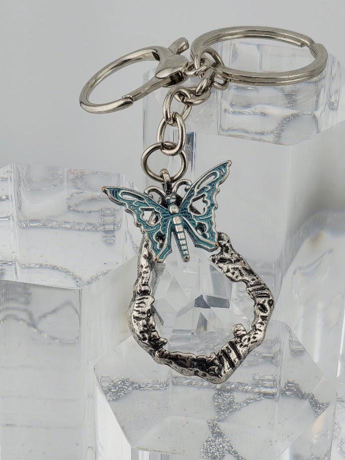 A silver keychain with a blue butterfly charm attached to it, resting on a clear crystal surface.