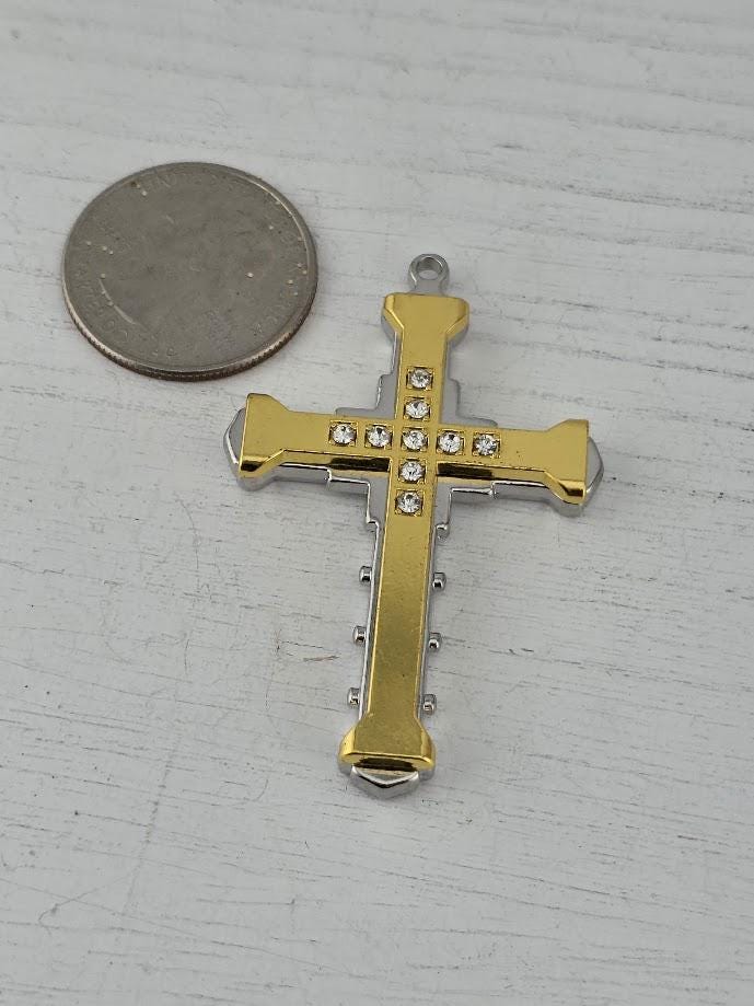 A gold and silver cross pendant with small diamonds on it, placed next to a silver coin on a white surface.