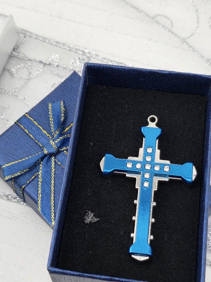 A blue and silver cross pendant is displayed in a blue gift box with a gold bow, placed on a white surface.