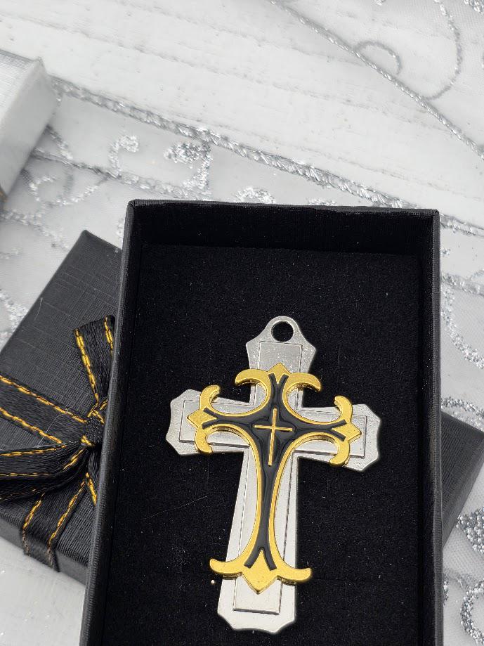 A silver and black cross-shaped ornament is displayed in a black box with a gold ribbon bow.