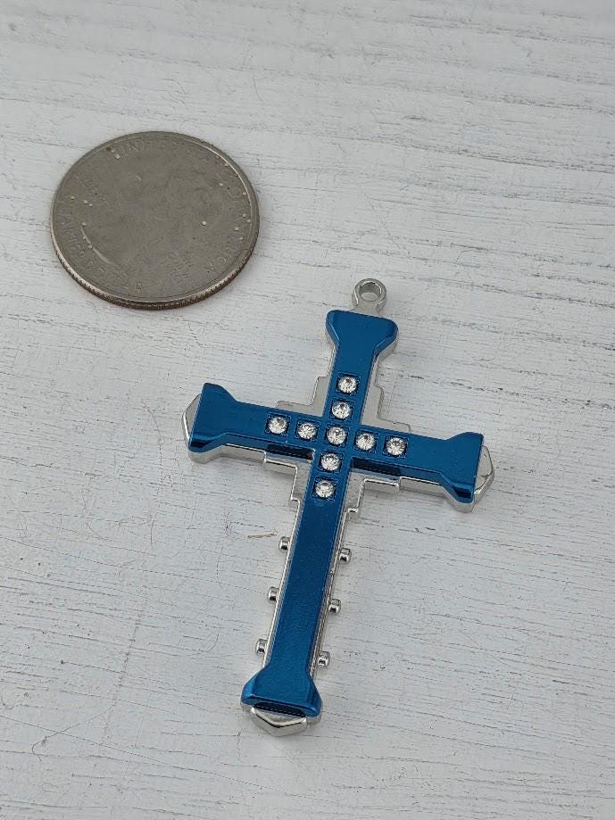 A blue and silver cross pendant is displayed in a blue gift box with a gold bow, placed on a white surface.