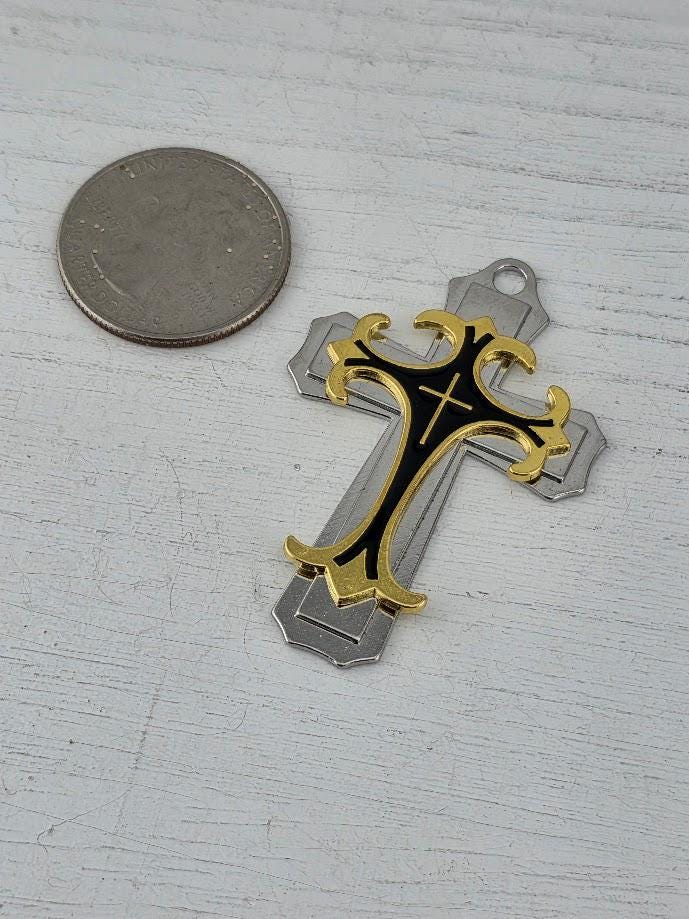 a silver cross-shaped pendant with a gold design, placed next to a silver coin on a white surface.