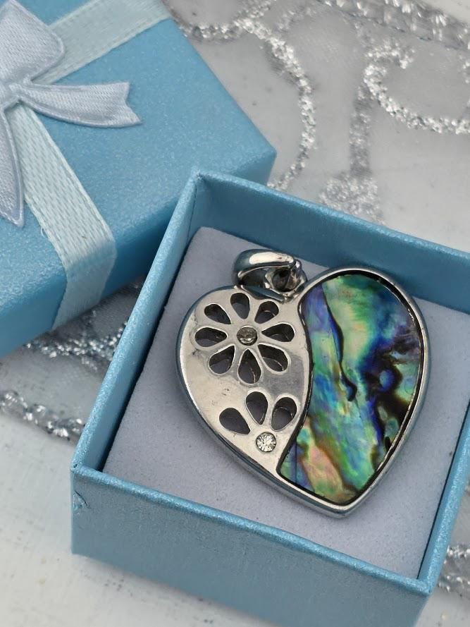 A heart-shaped pendant with a floral design and a gemstone is displayed in a blue gift box.