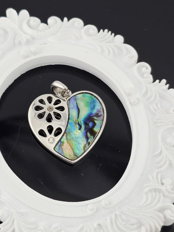 A silver pendant with a heart-shaped design and a colorful, iridescent stone in the center, displayed against a white ornate frame.