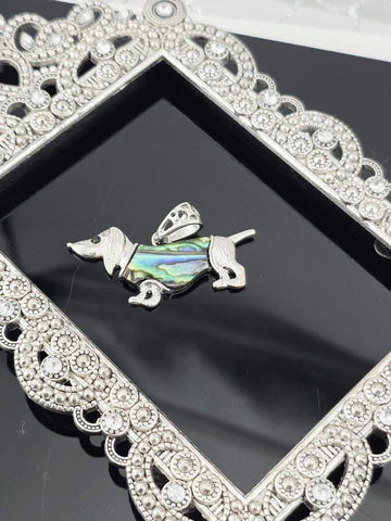 A silver-toned pendant in the shape of a dog, with a colorful iridescent design, is displayed in a decorative silver frame.