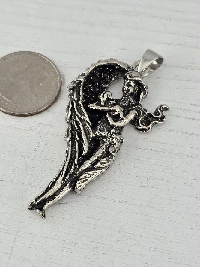 A silver pendant in the shape of a winged woman is displayed in a white box with a black interior.