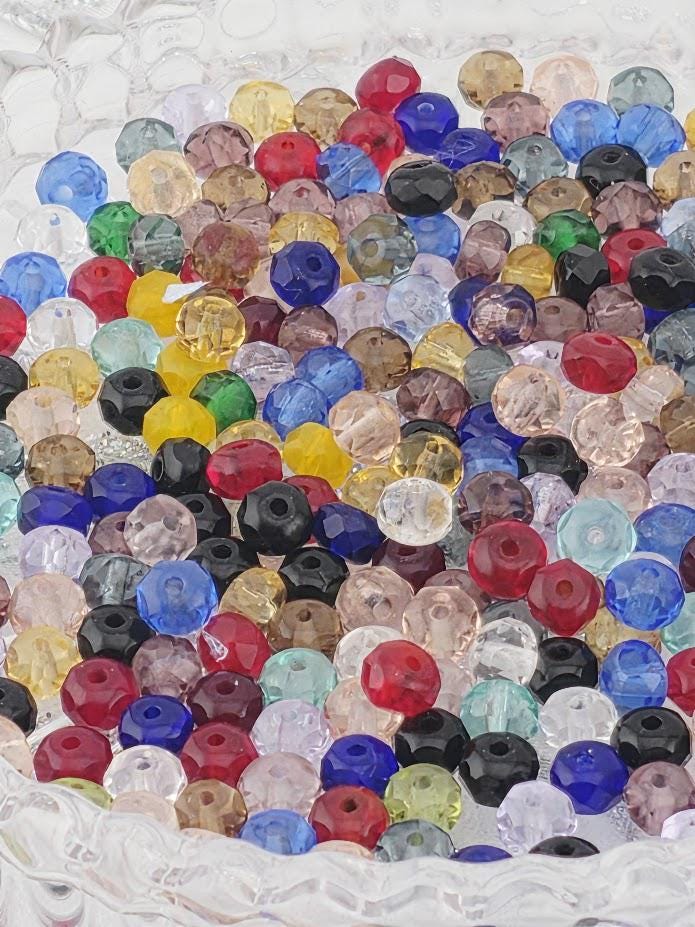 The image is a close-up of a collection of colorful glass beads, including clear, blue, red, yellow, and multicolored glass beads, arranged in a visually appealing manner.