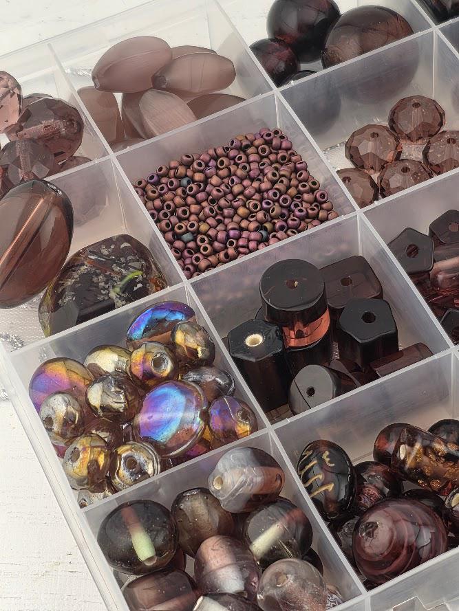 A collection of various beads and glass objects, including glass beads, glass beads, and glass beads, arranged in multiple compartments or containers.