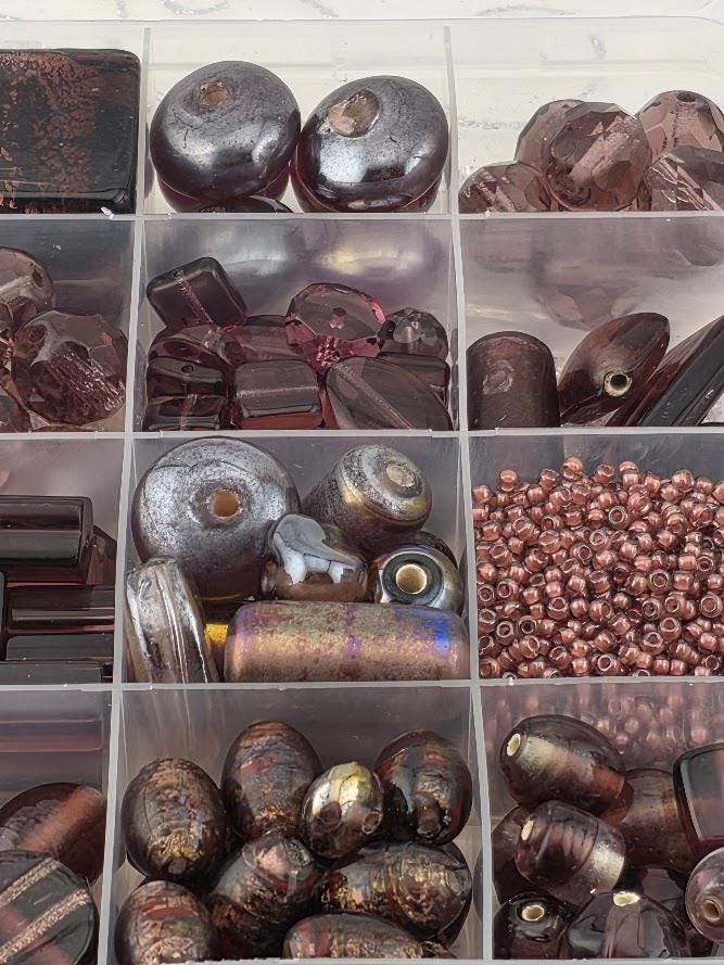 A collection of various beads and glass objects, including glass beads, metal beads, and glass beads, arranged in a clear container.