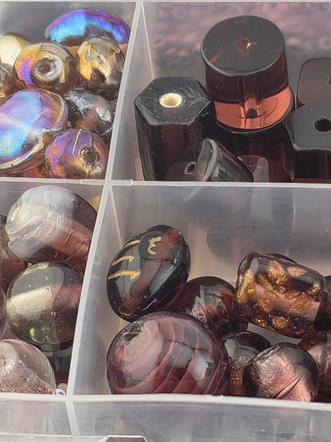 A collection of colorful glass beads and glass objects, including glass beads and glass containers, arranged in a clear plastic container.