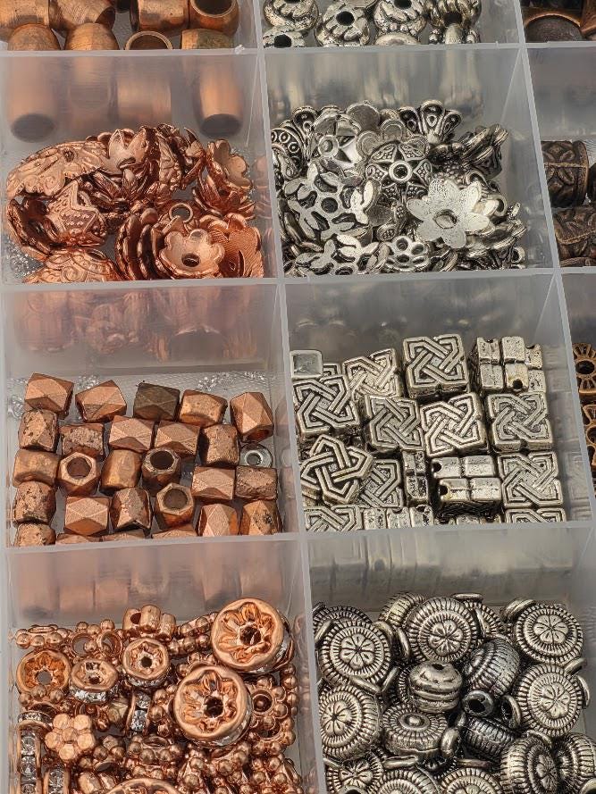 a collection of various beads and metal pieces, including copper-colored beads and silver-colored metal pieces, arranged in multiple compartments or containers.