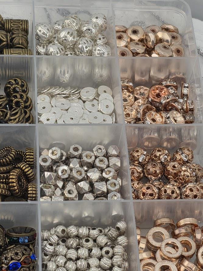 A clear plastic container filled with various beads and metal pieces, including gold, silver, and copper-colored beads.