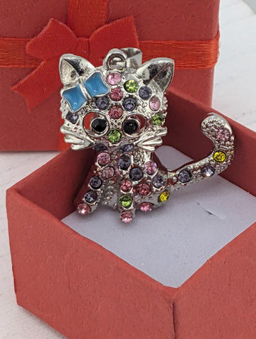 A silver cat-shaped pendant with colorful gemstones is displayed in a red gift box.