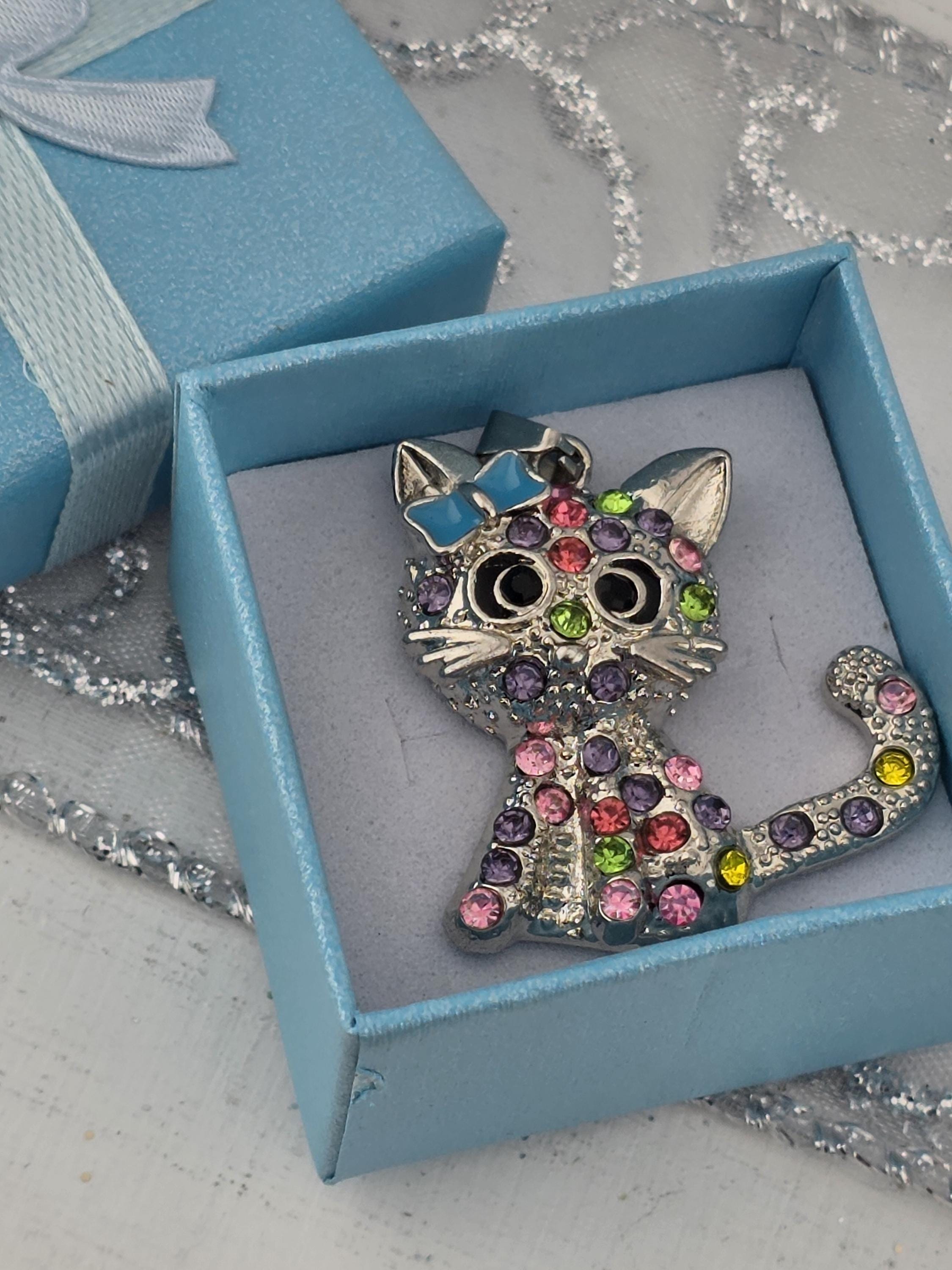 A decorative cat-shaped brooch with colorful gemstones is displayed in a blue gift box.