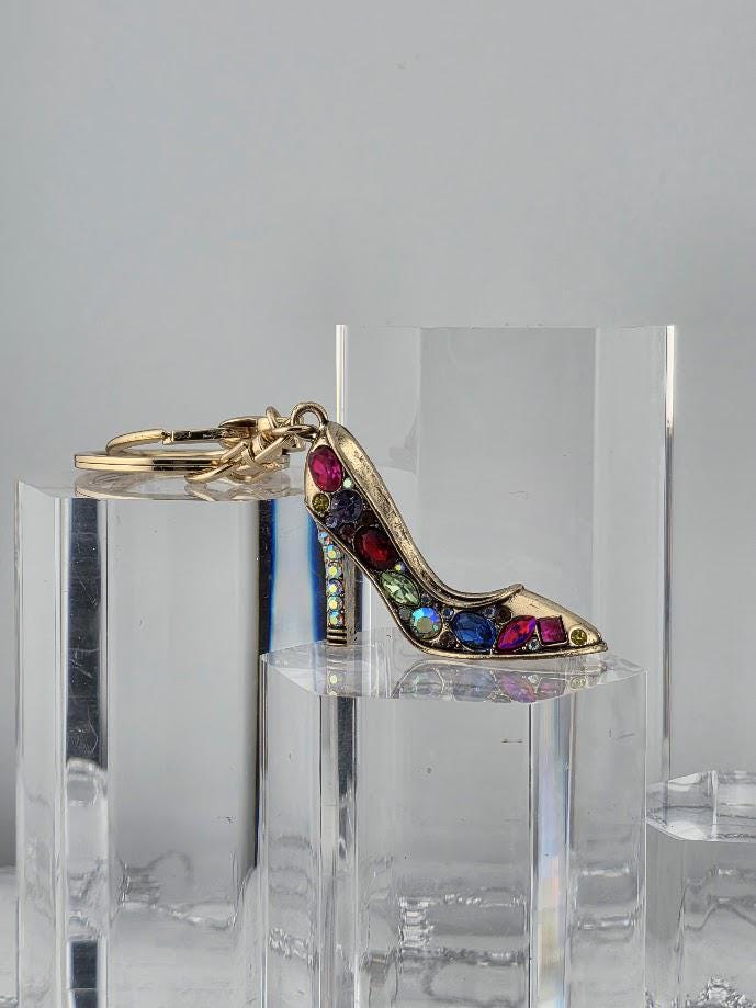 A keychain with a gold-colored shoe charm, adorned with colorful gemstones, is displayed in a black box.