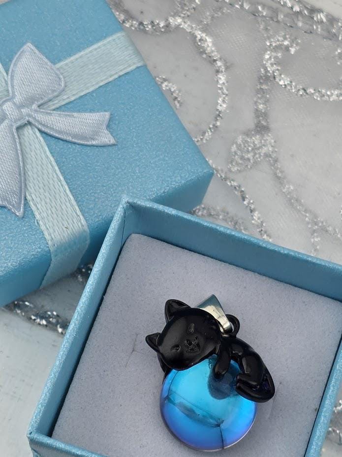 A small black cat figurine is sitting inside a red gift box with a red ribbon bow.