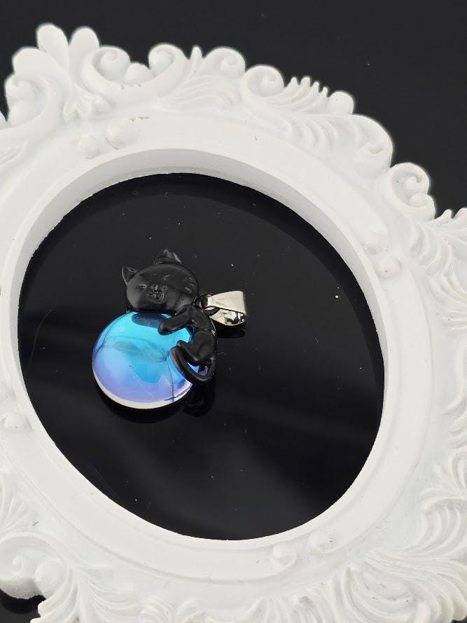 A pendant in the shape of a cat is displayed against a black background, with a white ornate frame surrounding it.