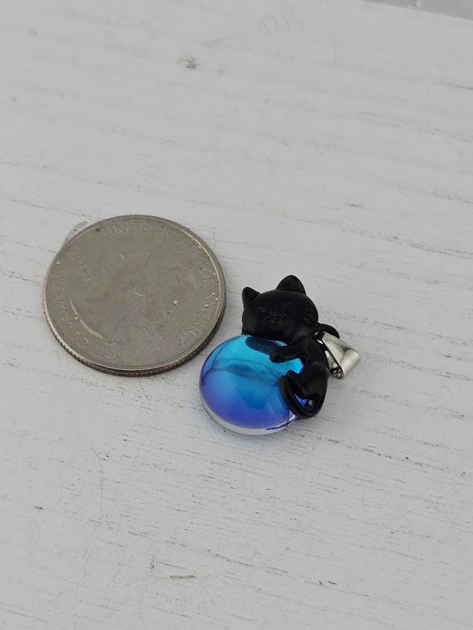A silver coin next to a blue glass bead with a black cat figure on it.